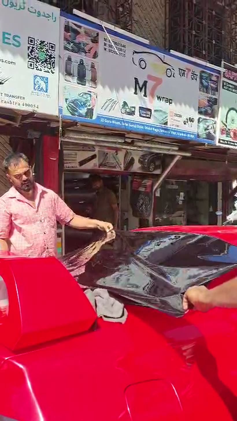 Two installers laying black roof film on a red car outside the M7WRAP shop